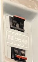 A gray electrical panel cover,
	with black-and-red circuit breaker handles visible